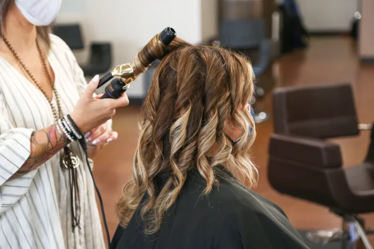 A student finishing a client blowout with a curling iron on the clinic floor
