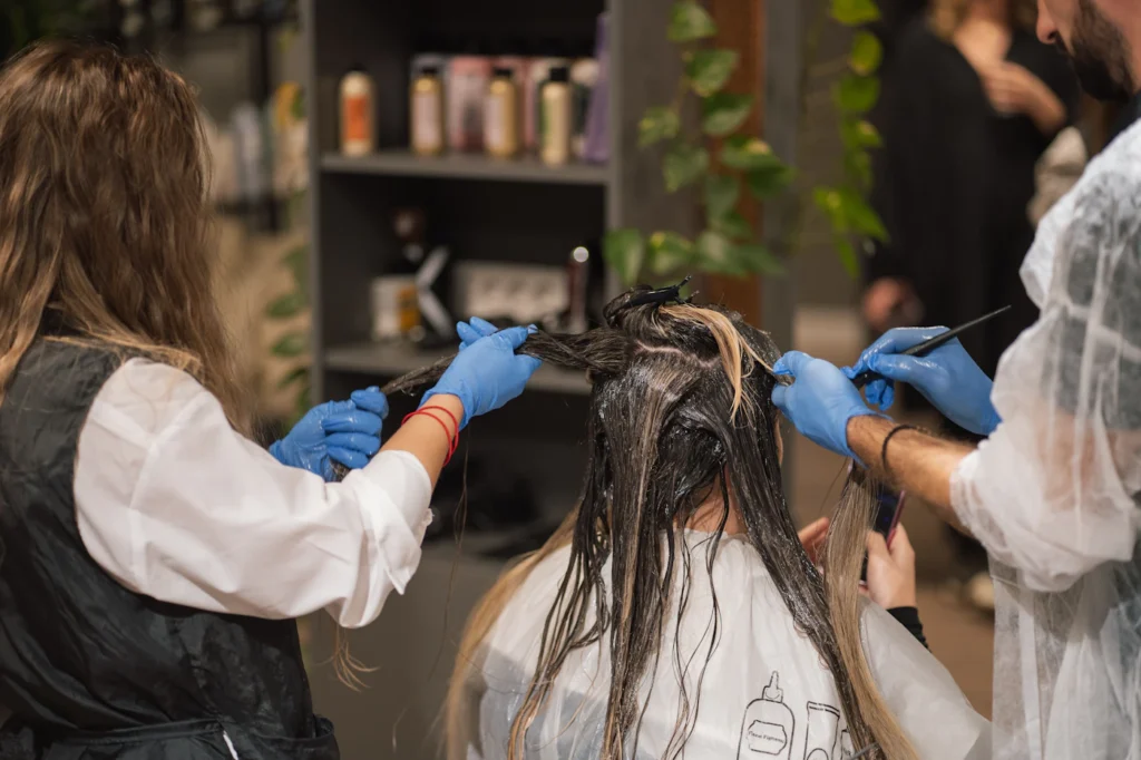 A cosmetology student applying colour to a client under supervision